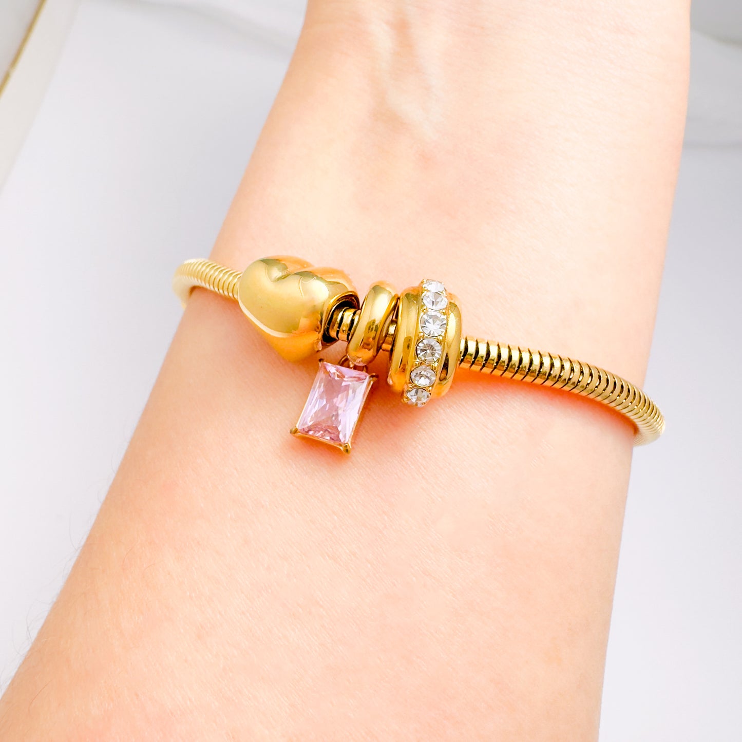 Gold bracelet with charms on a wrist against a light background